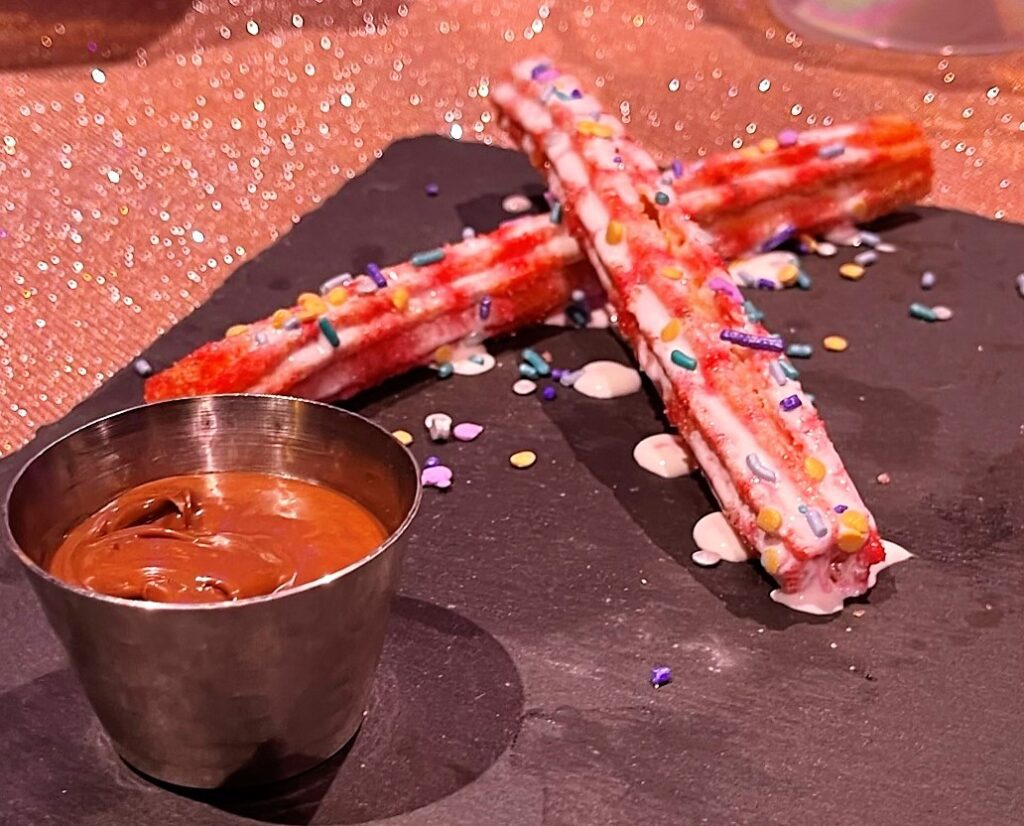 50th Celebration Churro:  Churro rolled in cinnamon and strawberry sugar, drizzled with marshmallow cream and shimmer sprinkles, and served with Chocolate-hazelnut dipping sauce.  (Available at Frontierland Churro Wagon)