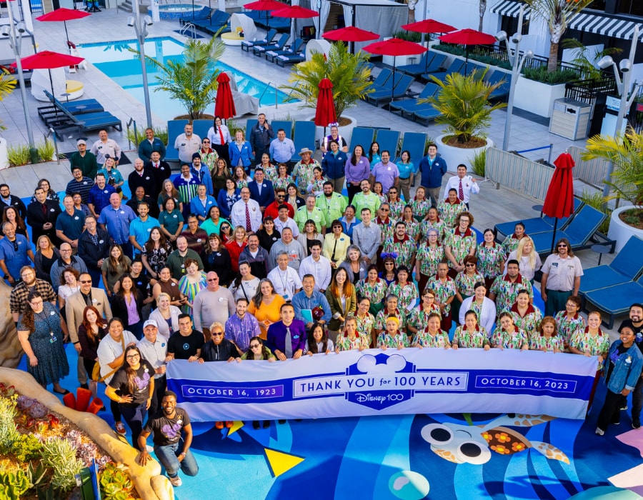 Cast members from DIsney's Paradise Pier Hotel pose on the pool deck in front of a "Thank You for 100 Years" banner