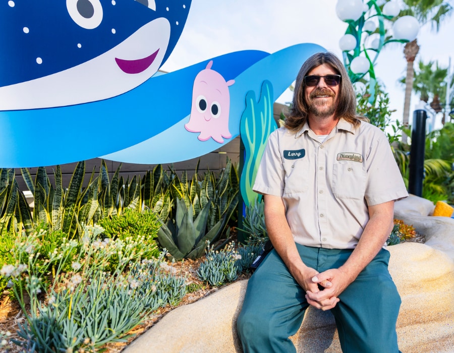 A Horticulture cast member sits on the edge of a planter filled with succulents, with "Finding Nemo" characters in the background