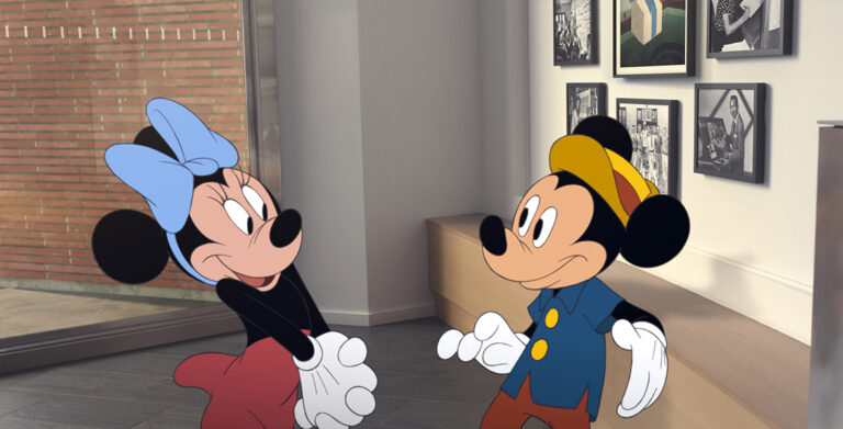 In a scene from the short film Once Upon a Studio, Minnie Mouse (left) clasps both hands and looks at Mickey Mouse (right). The two are standing in front of black and white portraits in the lobby of the Roy E. Disney Animation Building in Burbank, California.