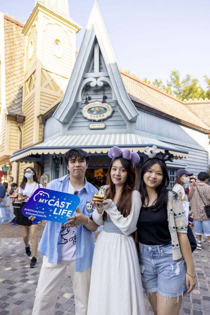 A group of cast members in Arendelle, one holding an Olaf-themed dessert and another holding a Cast Life photo prop