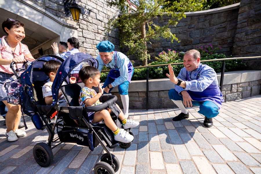 Cast members greet two young guests aboard a stroller entering World of Frozen