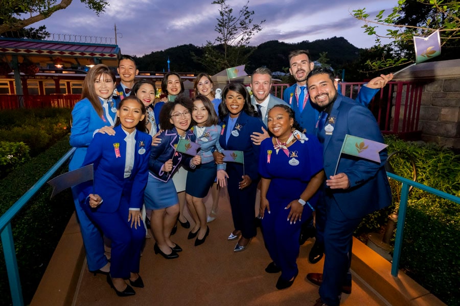 The Disney Ambassadors smiling and holing Arendellian flags as they stand outside the Fantasyland station of the Hong Kong Disneyland Railroad