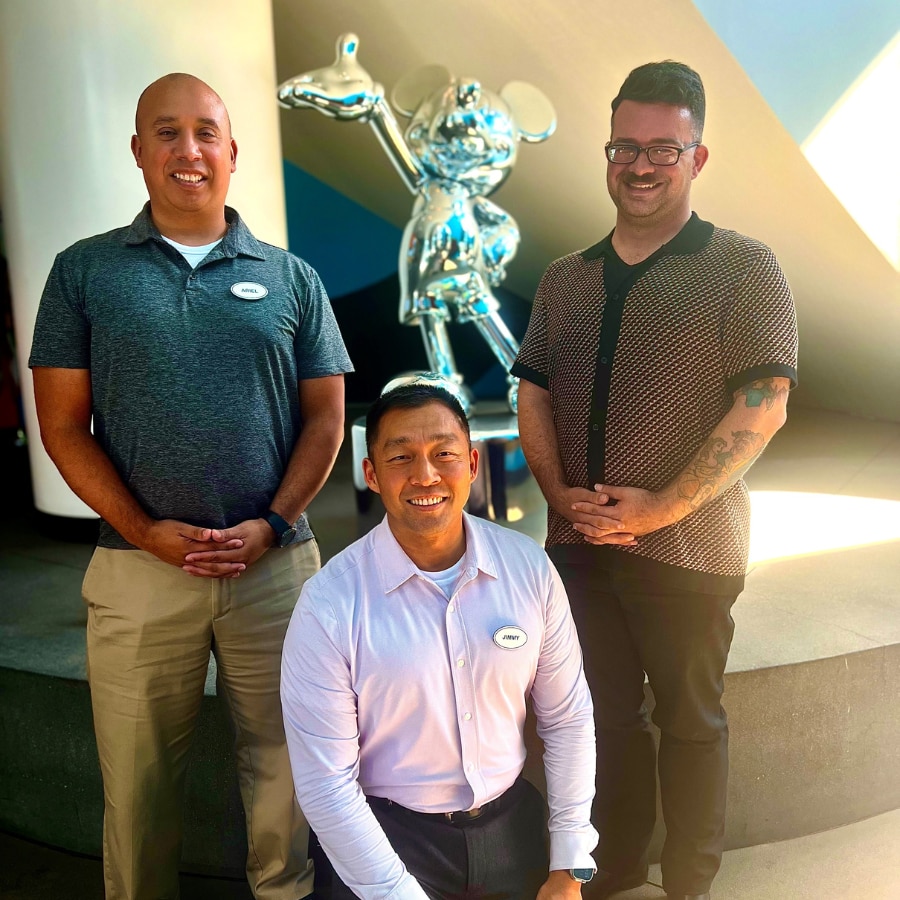 Three adults standing in front of platinum Mickey statue