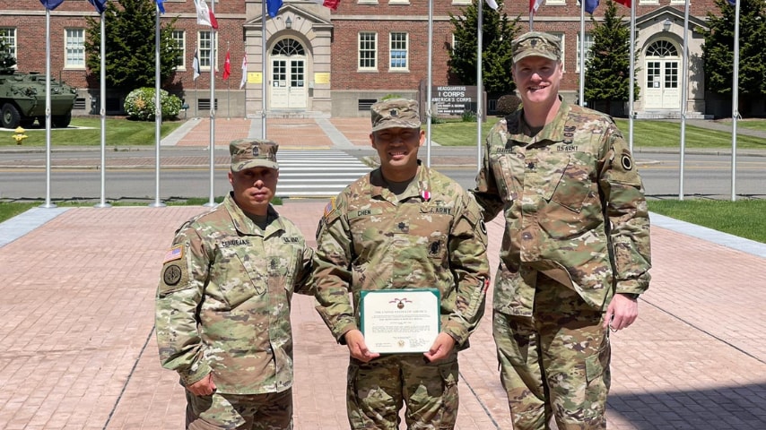 Three Army members pose with certificate in front of building