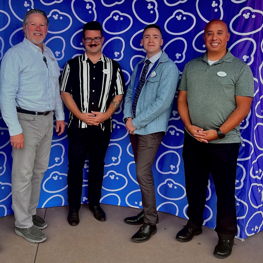 4 adults standing in front of blue name tag backdrop