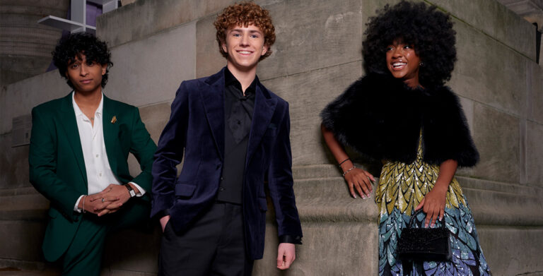 In an image from the world premiere for Disney+’s Percy Jackson and the Olympians, from left to right, Aryan Simhadri (Grover Underwood), Walker Scobell (Percy Jackson), and Leah Sava Jeffries (Annabeth Chase) are dressed to impress at the Metropolitan Museum of Art in New York City. Simhadri and Scobell look at the camera while Jeffries looks off to the left.