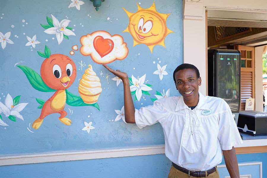 Cast member in front of a mural at Sunshine Tree Terrace featuring Orange Bird