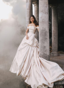 Available in a beautifully antiqued champagne tone as well as lovely, traditional ivory, this Belle-inspired ballgown finds its inspiration in the unforgettable lines of Belle's candlelit golden gown. This draped, off-shoulder satin gown is flawlessly textured, with ruching along the corseted bodice and gathered pickups across the voluminous skirt.