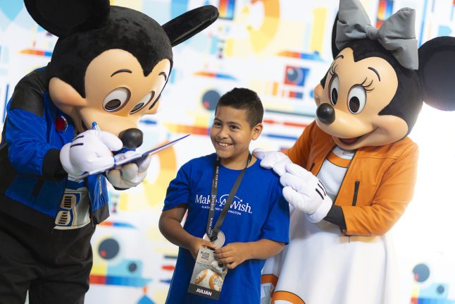 A child smiles with Mickey and Minnie as Mickey signs his autograph