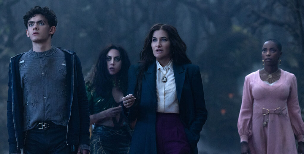 In a scene from Agatha All Along, (from left to right), Teen (Joe Locke), The Green Witch/Rio Vidal (Aubrey Plaza), Agatha Harkness (Kathryn Hahn), and Jennifer Kale (Sasheer Zamata) are standing together in a dark, foggy forest.