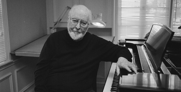 A black and white photo of John Williams sitting at the piano.