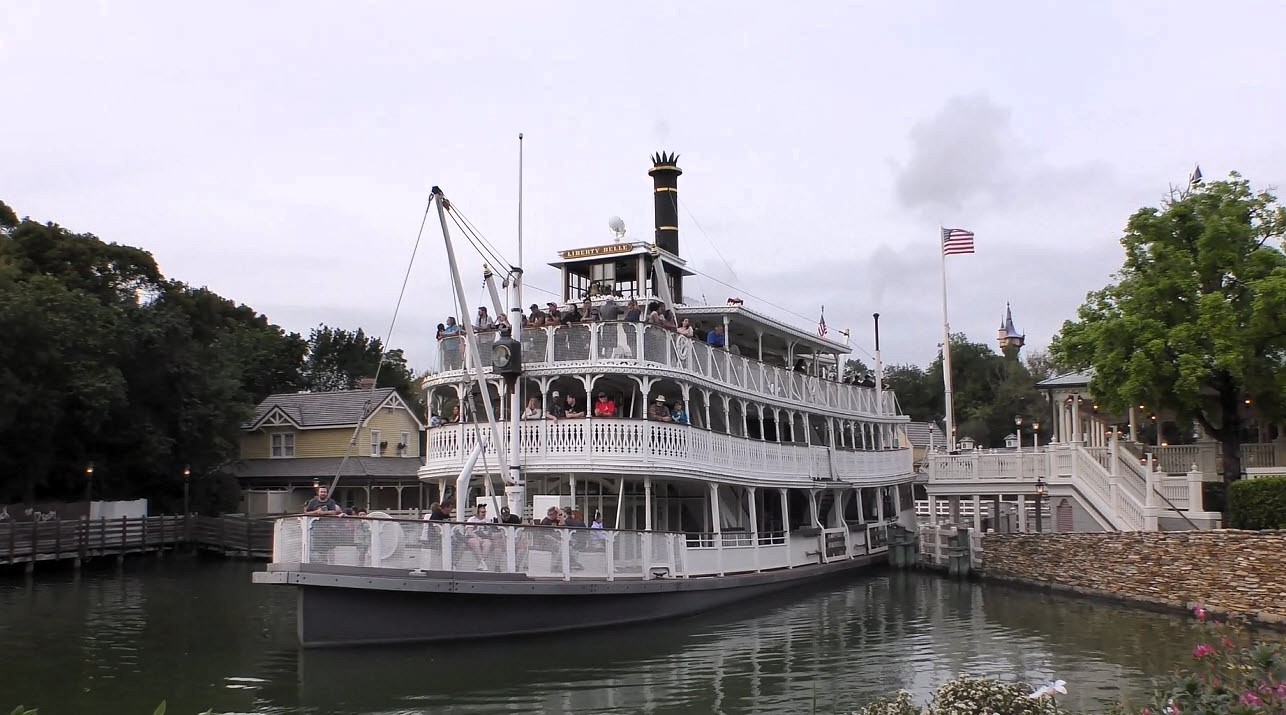 The Liberty Belle Riverboat, a majestic white paddlewheel vessel, glides gracefully along the Rivers of America at Magic Kingdom, showcasing its iconic vintage design and timeless charm.