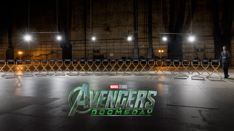 Twenty-seven directors chairs bearing the names of the Avengers: Doomsday cast members appear side by side in a vacant studio. Disney Legend Robert Downey Jr., wearing a gray suit, a white dress shirt, and a tie, stands next to a chair and points down at his name.